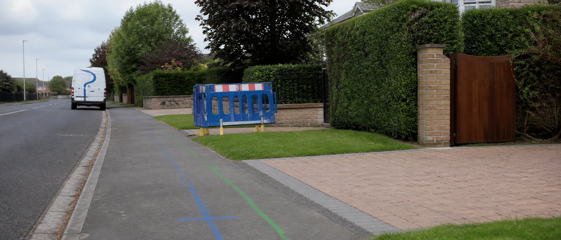 Marked buried pipe route beside a tidy suburban driveway before excavation